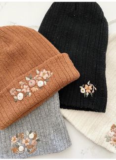 three beanies with flowers on them are laying next to each other and one has a flower embroidered on the side