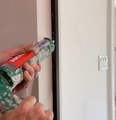 a person opening a door with a green and red spray bottle in their left hand