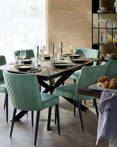 a dining room table set for four with blue chairs and plates on it, along with wine glasses