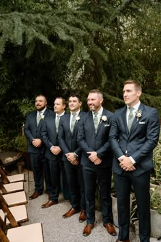 Groomsmen standing watching bride walk down the aisle Green Suit Blue Tie, Navy Blue Suit Green Tie Wedding, Navy Suit And Green Tie, Charcoal Mens Suit Wedding, Black Tuxedo With Green Tie, Eucalyptus Bridesmaid Dress With Navy Groomsmen, Navy Suits Groomsmen Color Schemes, Navy Blue Suit With Green Tie, Dark Navy Blue Groomsmen Suits