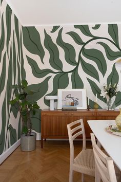 a dining room with green leaves painted on the wall and wooden table in front of it