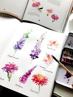 an open book with watercolor flowers on it and a person holding a paintbrush