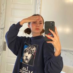 a woman holding up her cell phone to take a selfie in front of the mirror