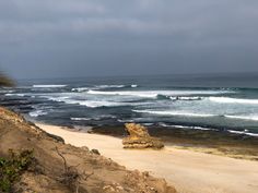 a sandy beach next to the ocean on a cloudy day with waves coming in and out