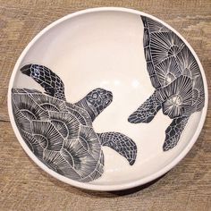 a black and white bowl with two turtles in the center on a wooden table top