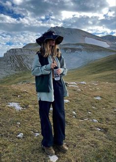 a woman standing on top of a grass covered field wearing a hat and holding a bottle