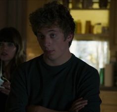 two people standing in a kitchen with their arms crossed and looking at something on the counter