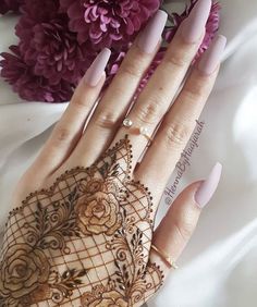 a woman's hand with henna on it and purple flowers in the background