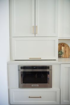 an oven built into the wall in a kitchen with white cabinets and cupboards behind it