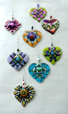 six heart shaped ornaments hanging from strings on a white surface with beads and bead