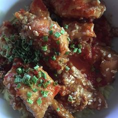 a white bowl filled with meat covered in sauce and green sprinkles on top of rice