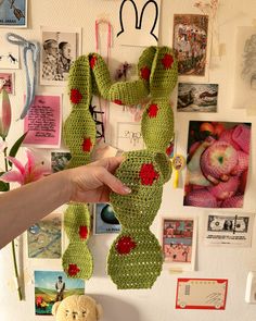 a person holding up a crocheted christmas stocking in front of a wall full of pictures