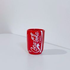 a coca - cola cup sitting on top of a white table next to a wall