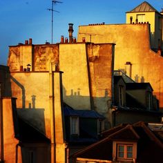 the sun is shining on some buildings and rooftops in an urban area with chimneys