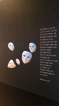 three white masks hanging from strings in front of a black wall with words written on it