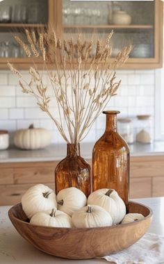 some white pumpkins are sitting in a bowl on the kitchen counter next to two brown bottles