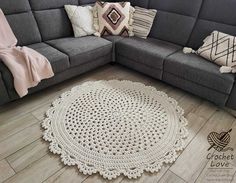 a crocheted rug on the floor in front of a gray couch with pillows