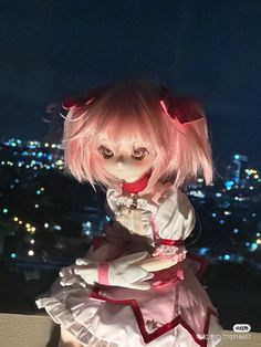 a doll with pink hair and white dress in front of a cityscape at night