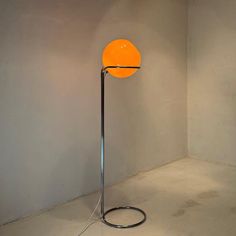 an orange lamp sitting on top of a floor next to a white wall with a black base