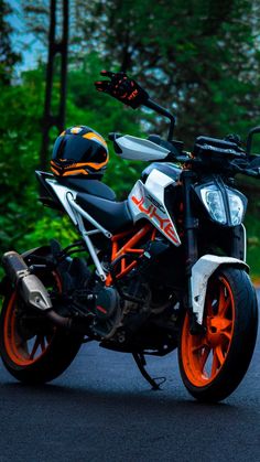 an orange and white motorcycle parked on the side of the road in front of some trees