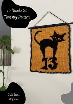 a crocheted black cat tapestry hanging on a wall next to a vase with a plant