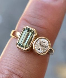 a close up of a person's hand holding a ring with an emerald stone