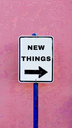 a street sign with an arrow pointing to the right and new things on it in front of a pink wall