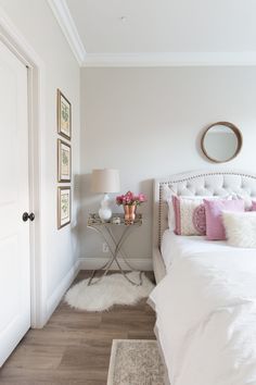 a white bed sitting in a bedroom next to a wooden table with flowers on it