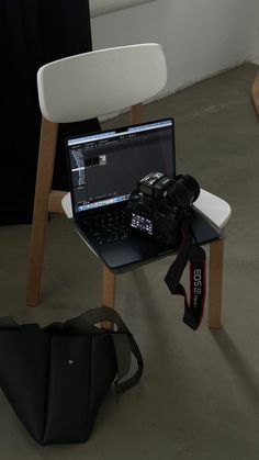 a laptop computer sitting on top of a wooden table next to a black bag and white chair