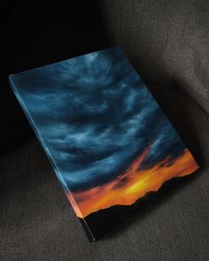 a book sitting on top of a couch next to a black chair with the sky painted in orange and blue