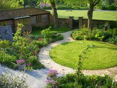 a circular garden in the middle of a lush green yard with lots of flowers and trees