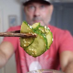 a man holding chopsticks over a jar filled with pickled cucumbers