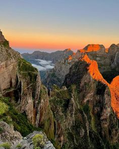 the mountains are covered in bright orange light and some clouds above them, as the sun sets