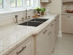 a kitchen with white cabinets and marble counter tops, along with a black double sink