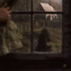 a person standing in front of a window looking out at a house and trees outside