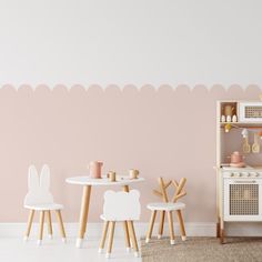 a child's play room with pink walls and white furniture, including a wooden table and chairs