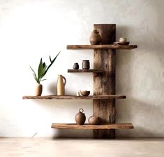 three wooden shelves with pots and vases on them in front of a white wall