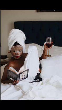 a woman laying in bed while holding a book and wine glass next to her face