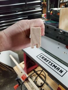 a hand holding a piece of wood in front of a machine that is being worked on