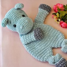 a crocheted blue stuffed animal laying on top of a table next to flowers