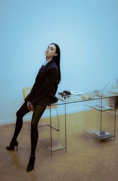 a woman sitting at a glass table with her legs crossed and looking up to the sky