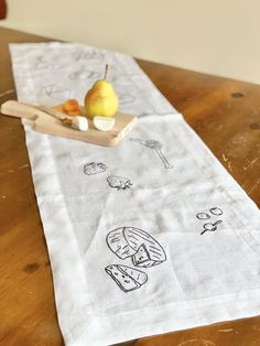 a wooden table topped with a white cloth covered in cartoon drawings and fruit on top of it