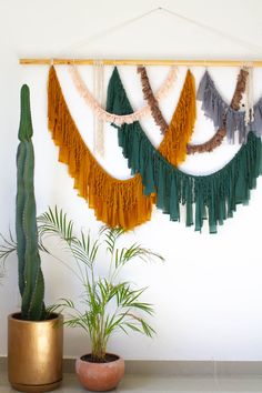 there is a potted plant next to a wall hanging with tassels on it