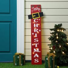 a merry christmas sign next to two presents on the grass near a blue front door