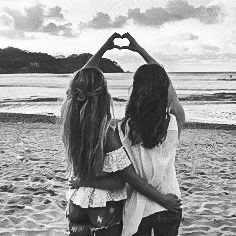 two girls making a heart shape with their hands on the beach