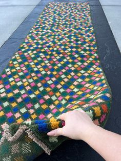 a person is holding onto a colorful blanket on the ground with one hand and touching it