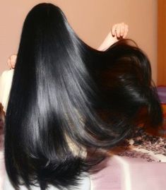 the back of a woman's head with long black hair laying on a bed