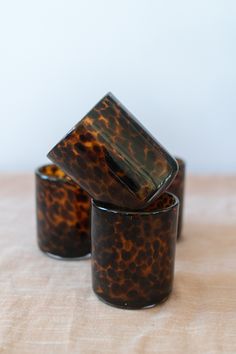 three brown and black cups sitting on top of a white tablecloth covered table cloth