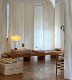 a living room with white curtains and wooden tables in the center, along with two lamps on either side of the table