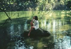 a woman sitting on top of a rock in the water